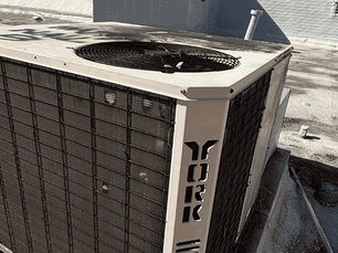 Outdoor air conditioning unit, labeled "York", on a concrete rooftop. Sunlit with shadow patterns. Industrial setting with sparse surroundings. This photo was taken by The Service Pros of a HVAC maintenance Tampa Bay.