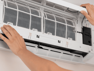 Hands opening a white air conditioner panel for maintenance and checking indoor air quality, revealing interior filters. The setting is a light-colored room.