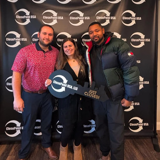 Two men and a woman stand in front of a backdrop holding a key that says "Just Closed!"