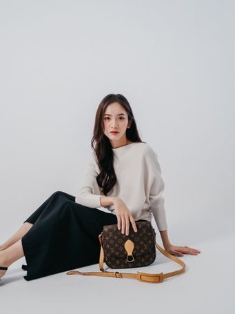 Woman in a white top and black pants sitting with a Louis Vuitton handbag.