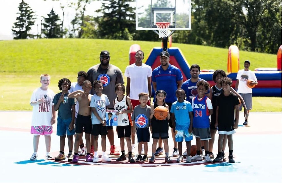 A group of kids and Detroit Pistons representatives pose together on an outdoor basketball court during the Motor City Crews' Neighbors Program Park Takeover, showcasing community unity, youth empowerment, and a love for basketball.