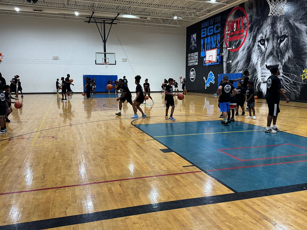 A group of young athletes actively participating in basketball drills on a gymnasium court during the Detroit Pistons x 3C Sports Camp. The kids, wearing matching black t-shirts, are engaged in various skill-building exercises while coaches provide guidance. The wall in the background features a large mural with a lion and the words “Unity in the Community,” symbolizing teamwork and empowerment.