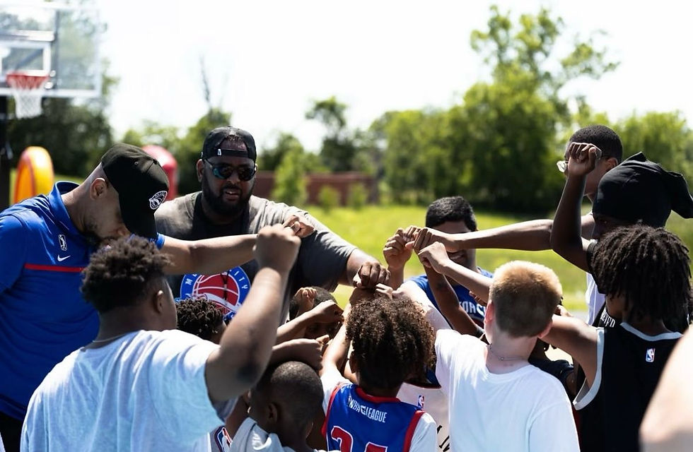 Motor City Cruise coaches and a group of kids join hands in a spirited team huddle on an outdoor basketball court during the Neighbors Program Park Takeover in Detroit.