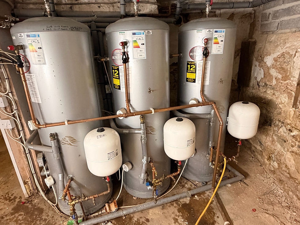 Three hot-water storage cylinders with expansion vessels and connected pipework in a plant room.