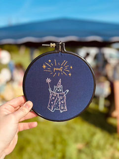 embroidery of a cat dressed as a wizard that says "poof"