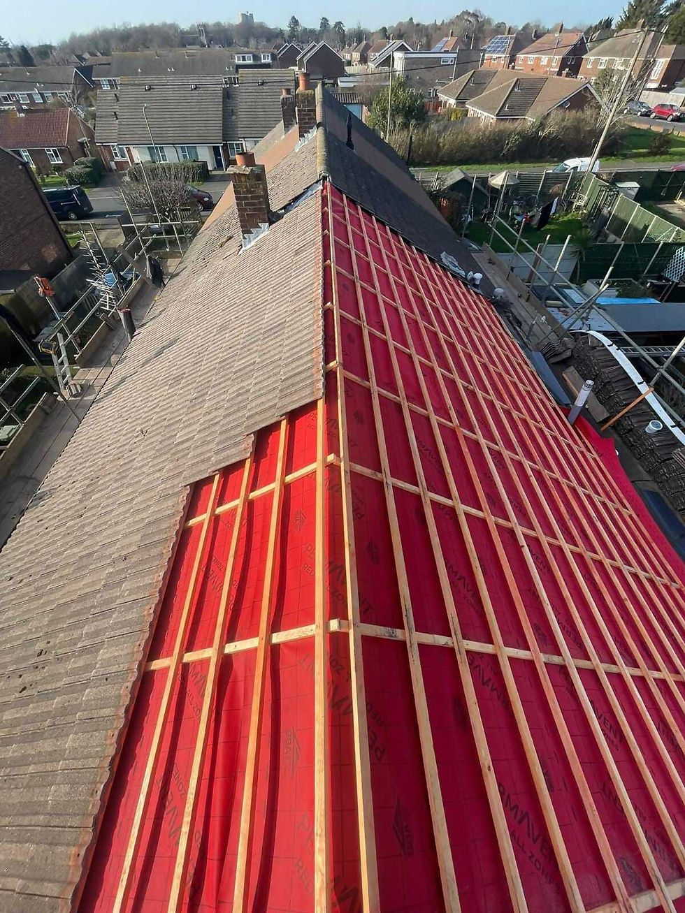 Red roof membrane and timber battens fitted alongside existing roof tiles on a UK home