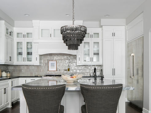 A white kitchen with taupe backsplash, black countertops, and gray barstools.