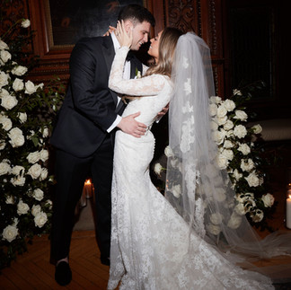 groom goes in for a kiss from his bride in front of a fireplace