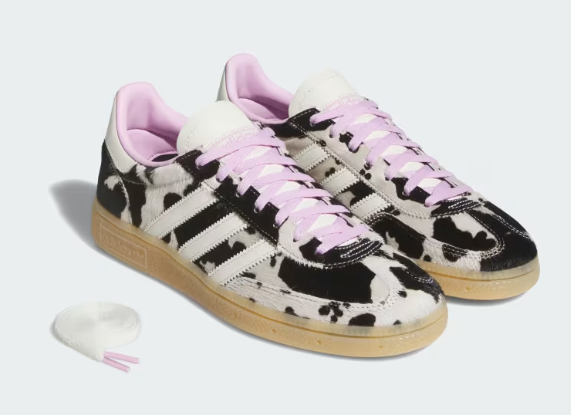 Pair of black-and-white cow-print sneakers with pink laces and gum soles on a white background, plus a loose lace tip.
