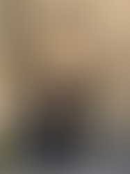 A person in a short beige trench coat and sunglasses stands against a stone wall holding a tan purse, exuding a chic, urban vibe.