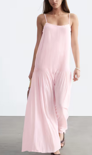 Woman in a pale pink sleeveless maxi dress stands against a white background, posing calmly on a gray floor.