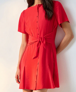 Woman in a bright red button-front dress with tied waist, standing against a plain white wall.