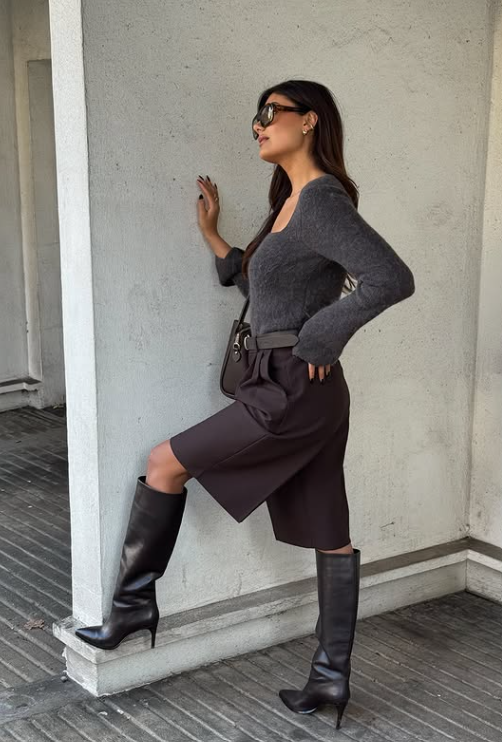 Sleek black knee-high leather boots with stiletto heels styled with dark brown tailored shorts and a grey sweater – 8 shoe trends 2026