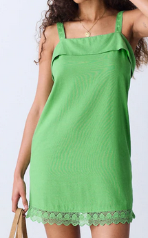 Woman in a bright green sleeveless dress with lace hem poses against a white background, holding a tan bag.