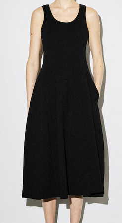 Person in a sleeveless midi black dress stands against a plain white background, minimalist and elegant.