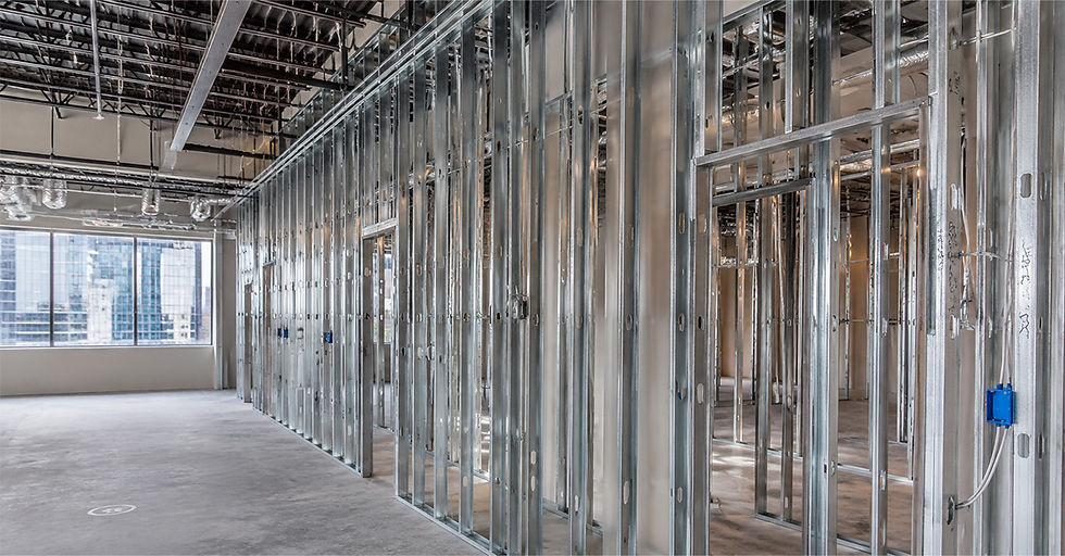 Unfinished office interior with steel wall framing, exposed ceiling, and large city-view windows, empty and bright