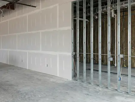 Unfinished commercial interior with drywall, exposed steel studs and concrete floor at a quiet construction site.