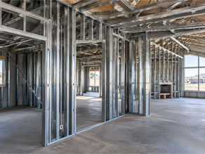 Unfinished house interior with exposed steel framing, empty rooms, large windows, and bright daylight.