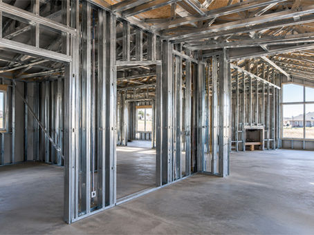 Unfinished house interior with exposed steel framing, empty rooms, large windows, and bright daylight.