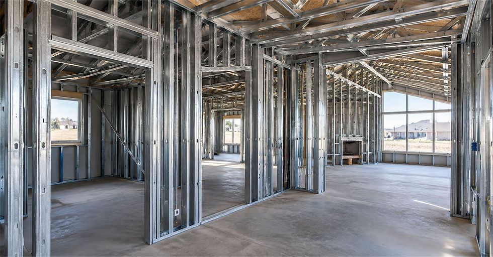 Unfinished house interior with exposed steel framing, empty rooms, large windows, and bright daylight.