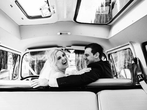 Happy couple seated inside VW Kombi van, looking back at photographer and smiling
