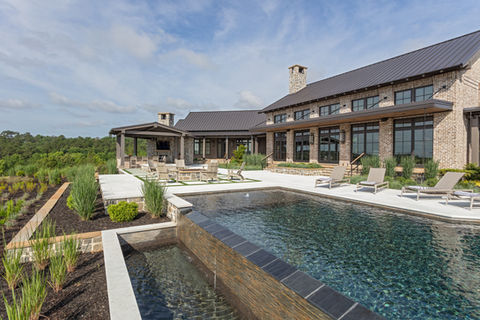 Exterior view of brick and stone custom, luxury mansion with landscaping and infinity pool
