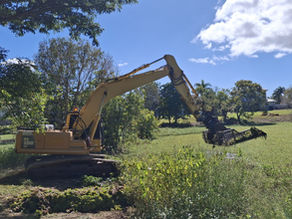 An excavator removes weeds from a weed covered lake