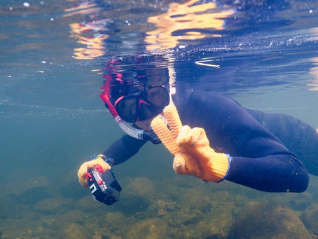 A snorkeler holds a camera whilst posing for the camera underwater