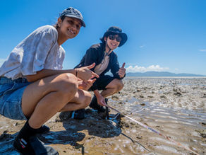 Two interns squat in a sandy area at low tide whilst holding a measuring tape