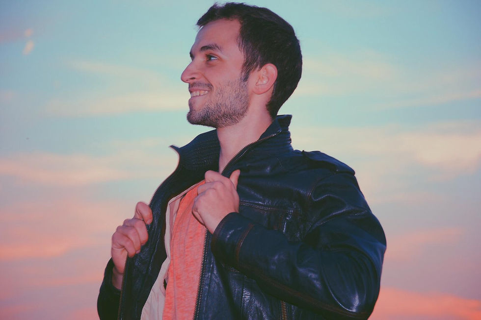 Ein lächelnder Mann in Lederjacke vor Abendhimmel.