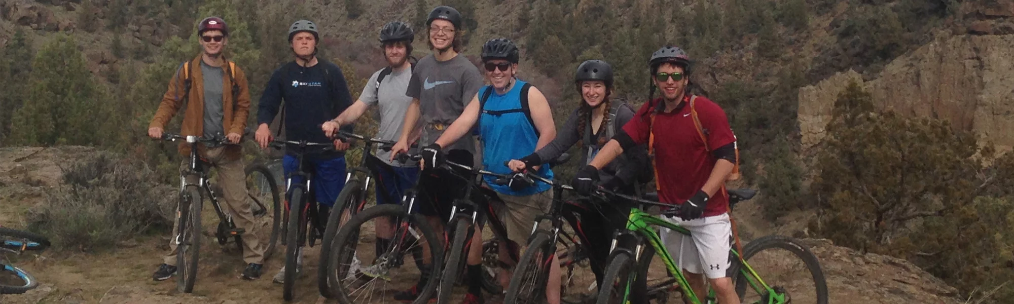 seven young adults standing on mountain bikes smiling