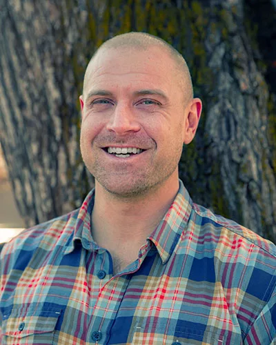 man smiling in front of a tree