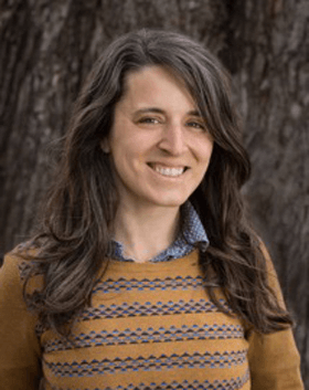 woman stands in front of a tree smiling