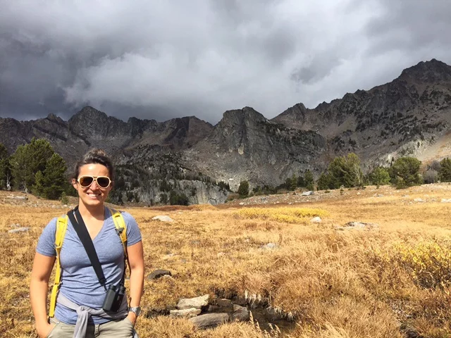 woman stands smiling in front of overcast skies and grey mountains