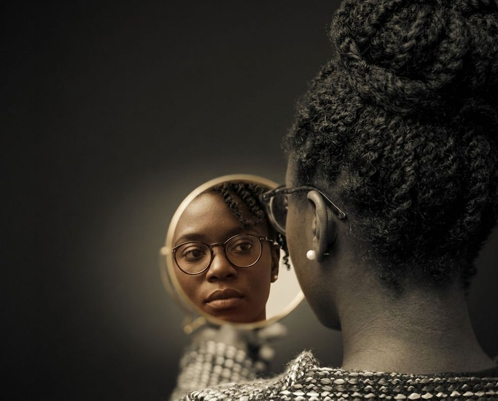 A reflective portrait of an African American woman gazing into a hand mirror. The image highlights the texture of her hair and the quiet, introspective moment captured in the reflection.