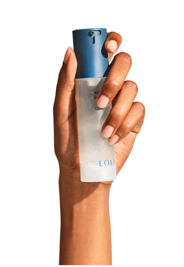 Hand holding a frosted bottle with a blue cap against a white background. The bottle has text starting with "LOL" visible near the base.