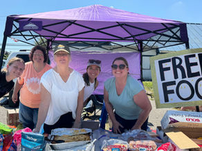 A group of volunteers standing under a tent offering free food and supplies to the community