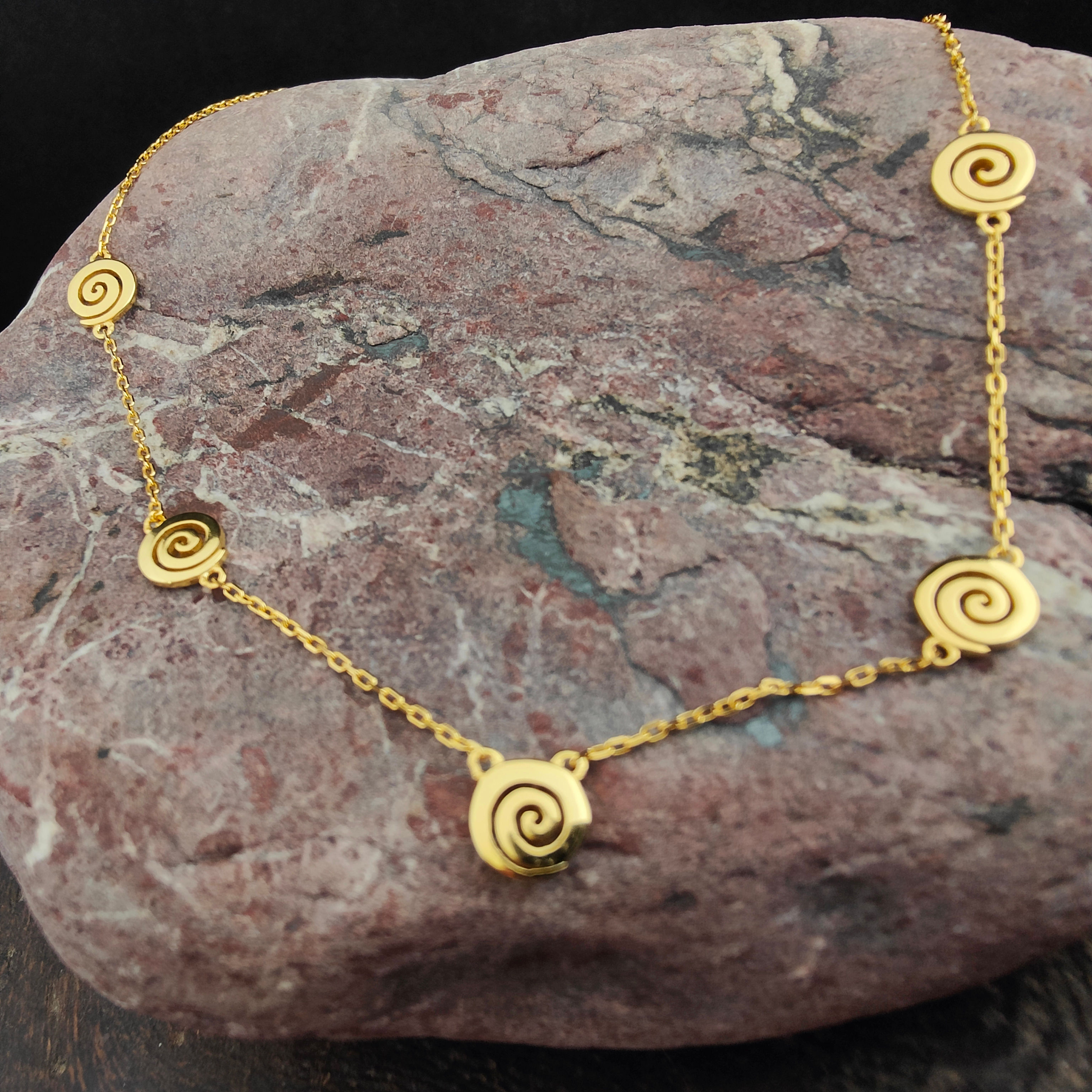 Gold necklace with spiral design on stone background. Thetistreasures