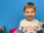 A smiling child at Trinity Lutheran, Church, School, and Childcare holding a children's book in front of a blue background