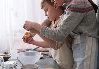 Young child focuses on cracking eggs into a mixing bowl, surrounded by baking tools and in