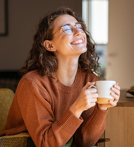 Portrait of joyful young woman enjoying a cup of coffee at home. Smiling pretty girl drink