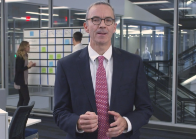 Man in a suit and glasses speaking in an office.