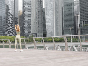A woman in a light green workout outfit stretching on a dock overlooking the water, preparing for a walk.