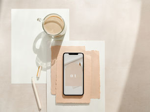 Flat lay of wedding planning essentials with phone, pen, and clear coffee mug on a white and peach background.