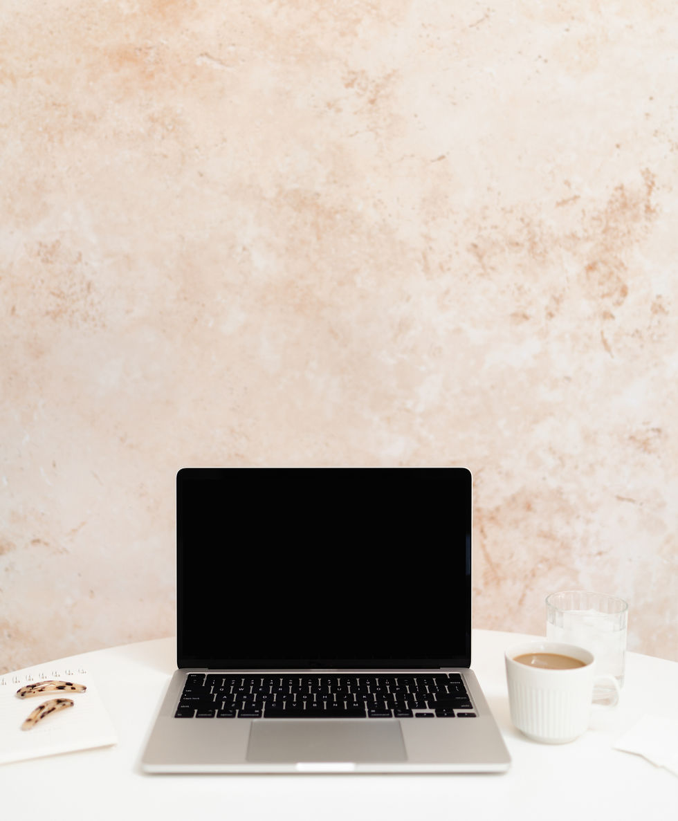 Laptop on peach and white desk with notebook and coffee, creating a calm wedding planning setup.
