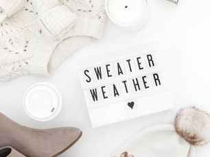 Flatlay of fall essentials on a white background, including a chunky sweater, boots, a to-go coffee cup, and a word board that says “Sweater Weather,” styled for a September reset mood.