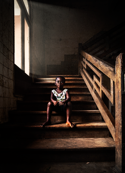 A poor kid seated on the stairs of an abandoned hospital in  Africa
