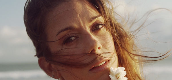 still from music video, where woman looking into a camera during golden hour on the beach