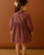 Back view of a young girl wearing a mauve dress with a single-button keyhole closure and ruffled neckline