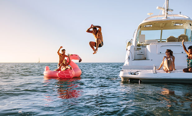 Man diving in the sea with friends sitting on yacht and inflatable toy. Group of friends e